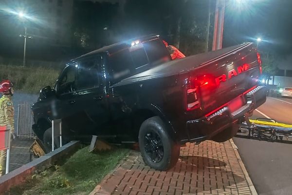 Imagem referente a notícia: Caminhonete bate em semáforos e fica pendurada em estrutura de farmácia em Cascavel